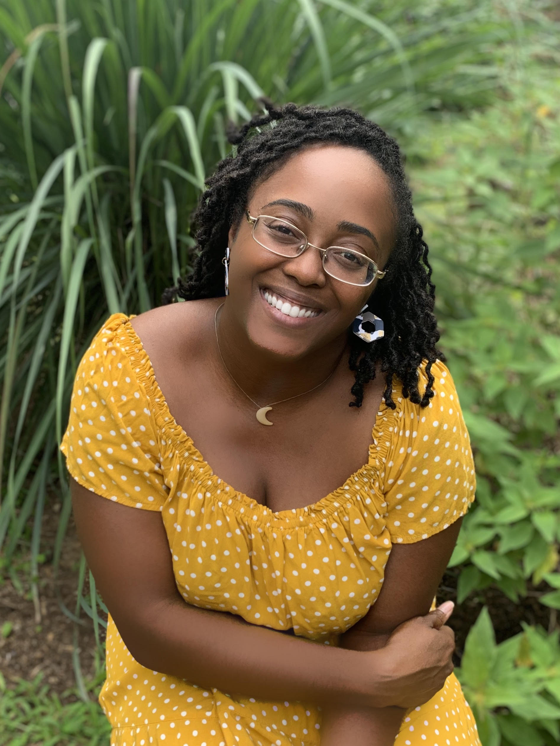 headshot of christina lynch taken at a downward angle with her wearing a yellow dress, and surrounded by green grassy background